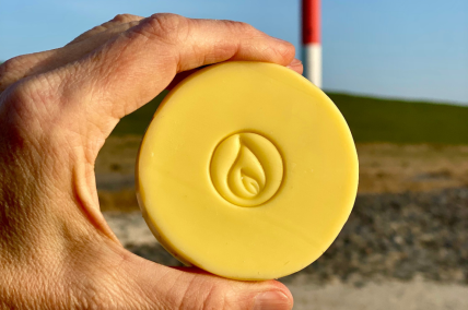 Eine Hand hält eine Naturseife namens Jadebusenseife mit Leuchtturm aus der Nordsee im Hintergrund