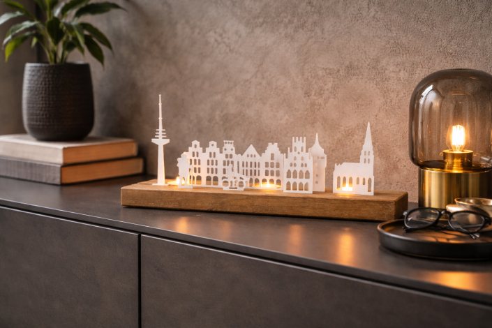 Die Skyline von Münster auf dem Eichesockel auf einem modernen Sideboard arrangiert mit einer Brille, Büchern und eine Tischleuchte aus getöhntem Glas.
