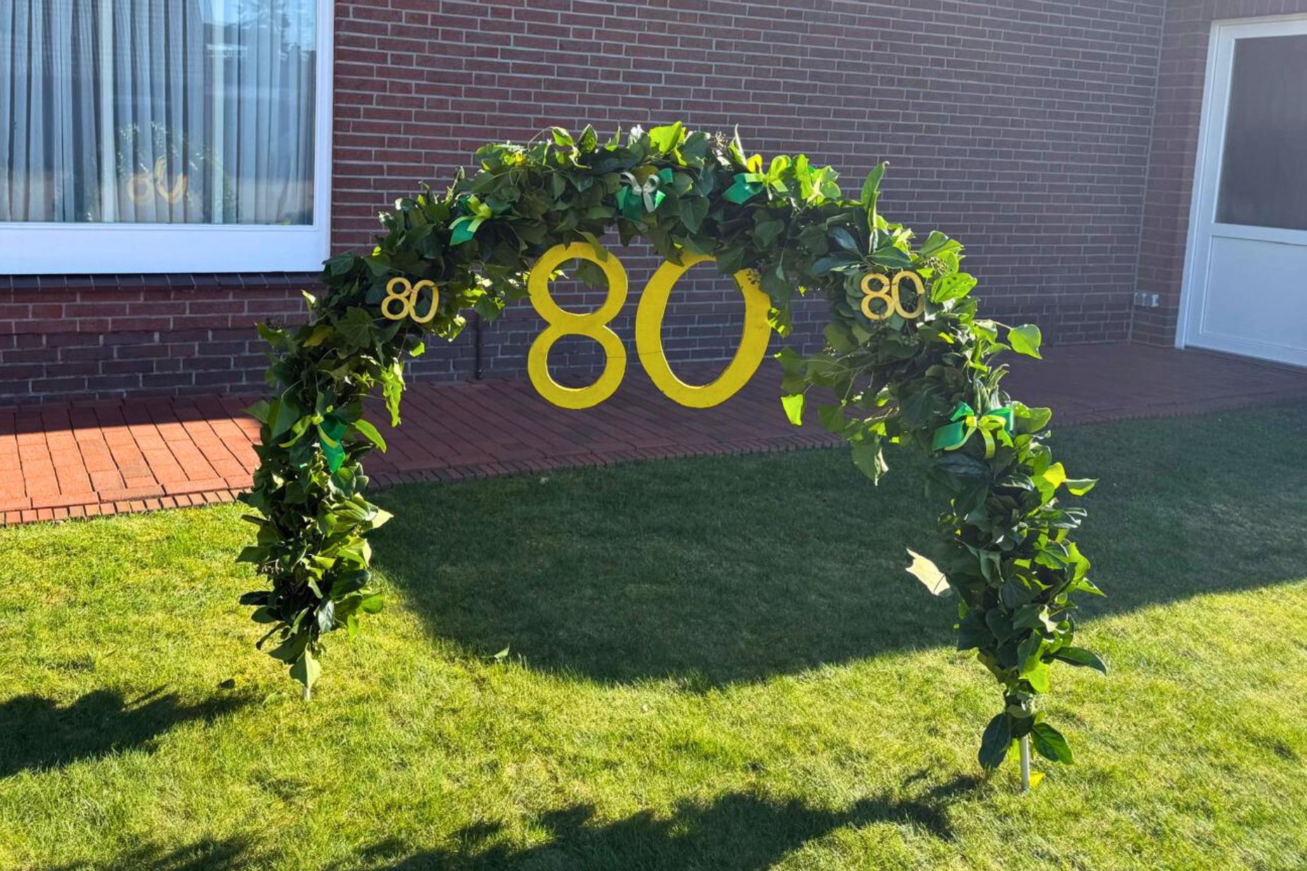 Ein Kranz aus Grünpflanzen mit einer 80 dran im Garten aufgestellt