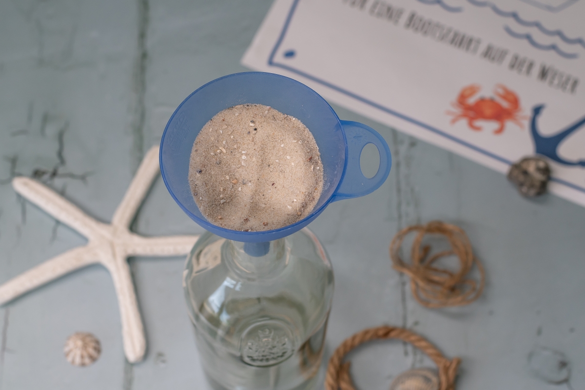 Sand wird mit einem Trichter in eine Flasche gef&uuml;llt. 